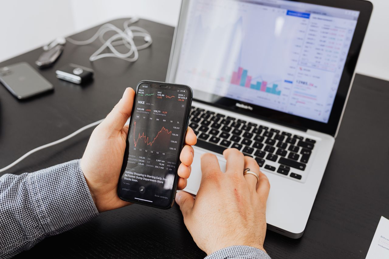 about-us Person analyzes stock data with a smartphone and laptop, indoors.